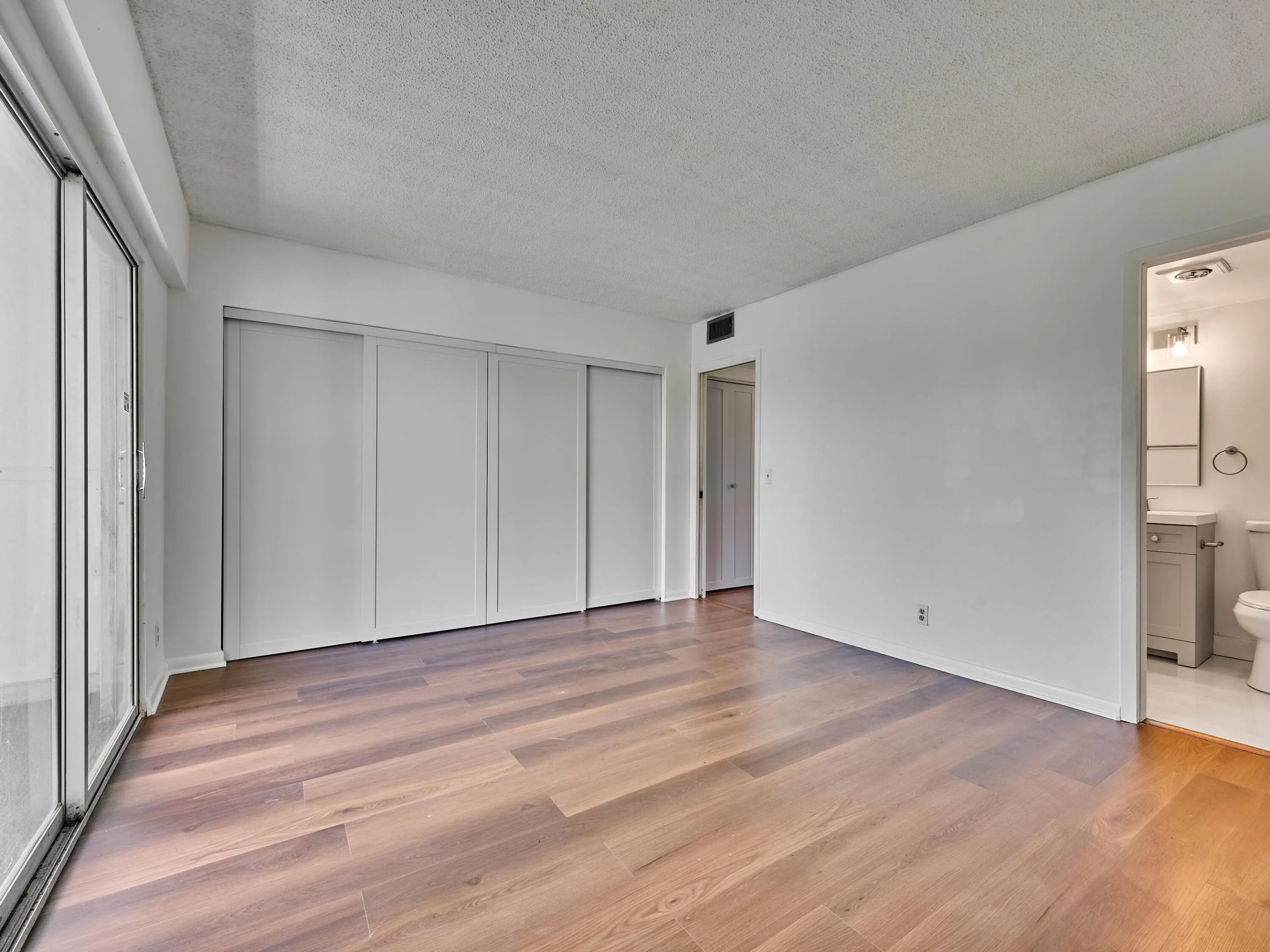 Spacious interior featuring wood-finish flooring, white walls, and a full wall of sliding door closets