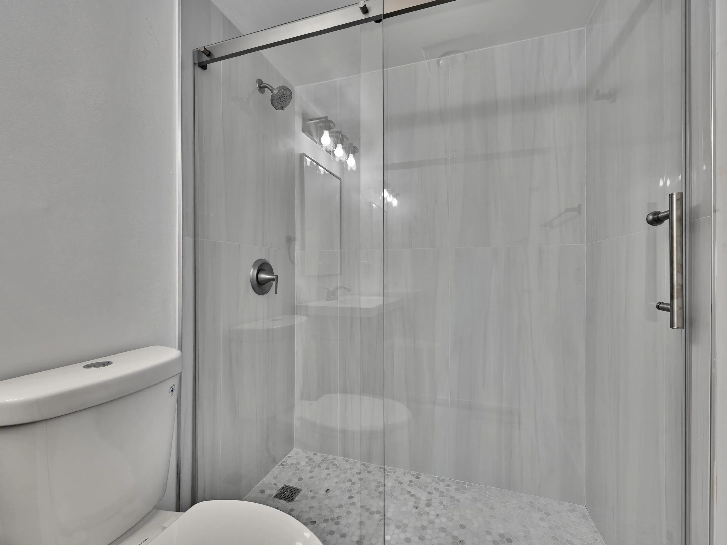 Glass-enclosed shower with brushed nickel hardware, light-toned tile surround, and a mosaic tile floor