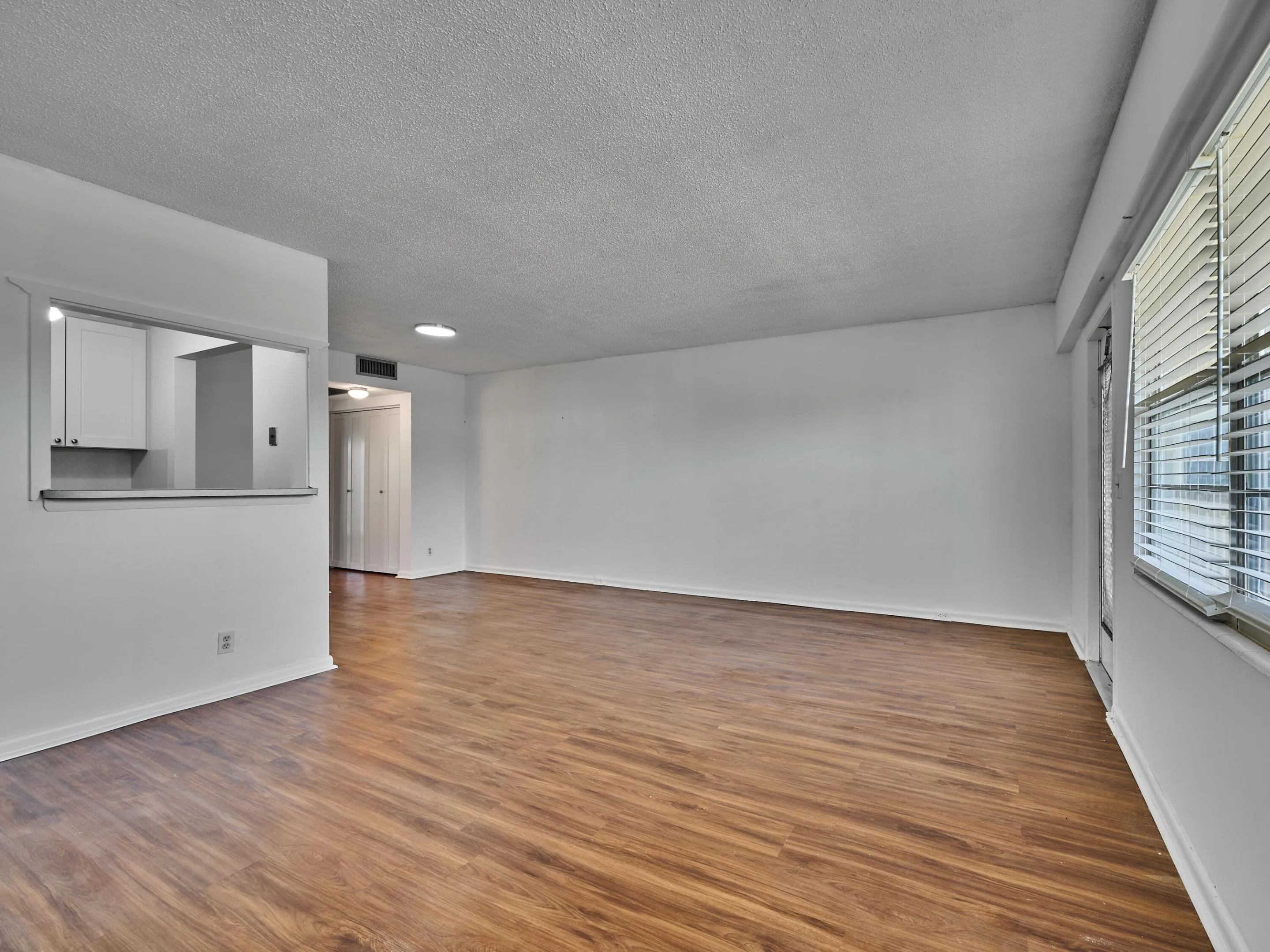 Open concept living area featuring wood-finish flooring, white walls, and a pass-through window to the kitchen