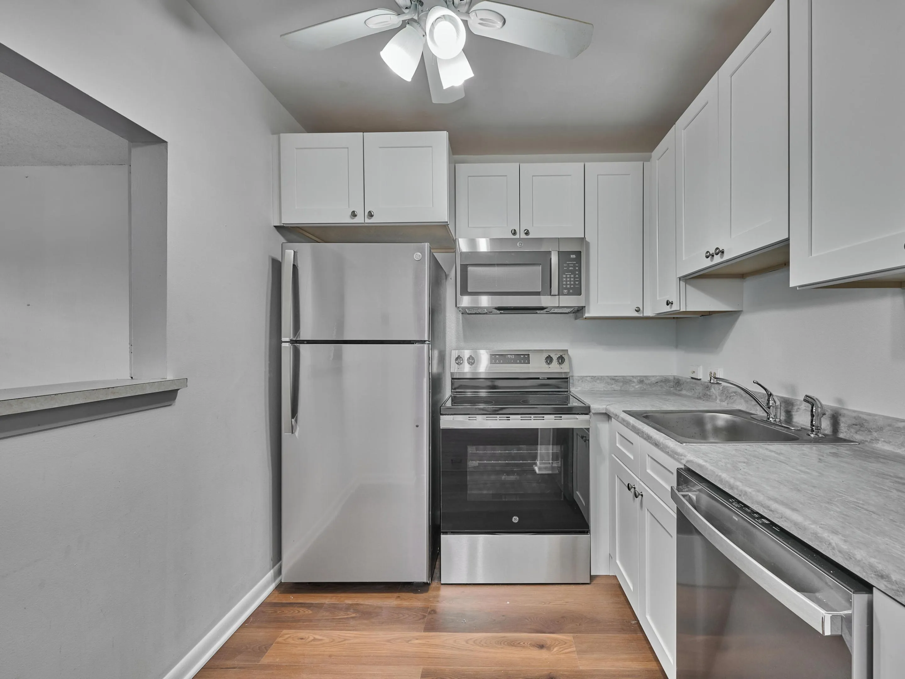 Kitchen featuring white cabinetry, stainless steel appliances, wood-finish flooring, a stainless steel sink, and a ceiling fan with integrated lighting