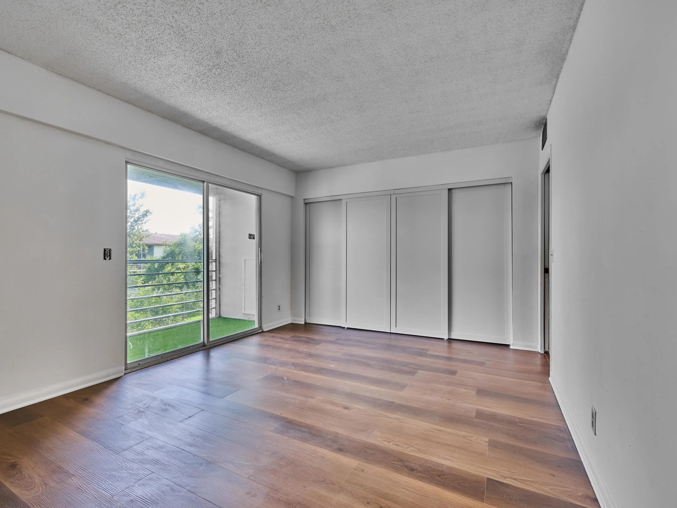 Room featuring wood-finish flooring, white walls, and a sliding glass door leading to a balcony