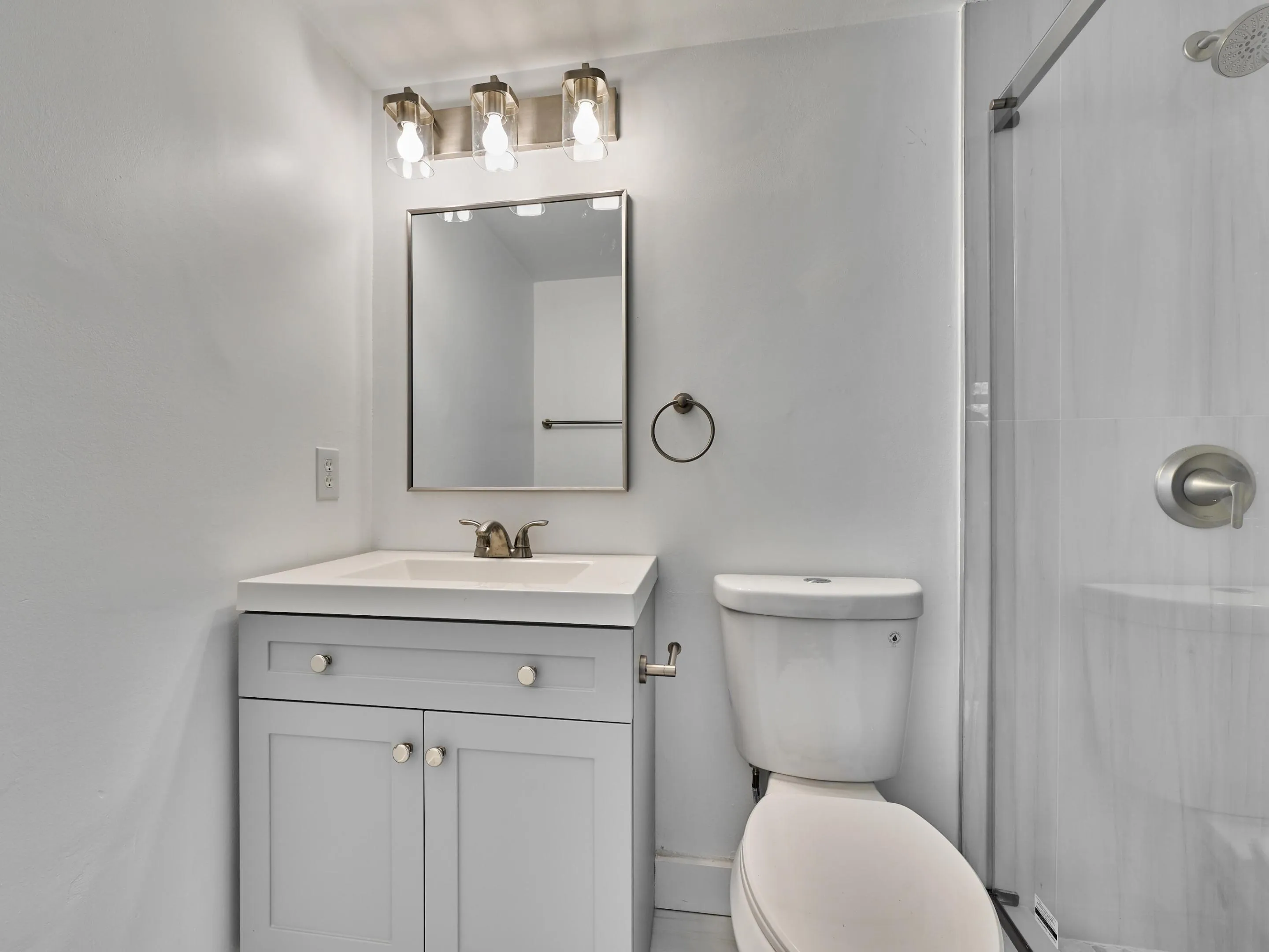 Contemporary bathroom featuring a light gray vanity with brushed nickel hardware, a white integrated sink, and a modern rectangular mirror