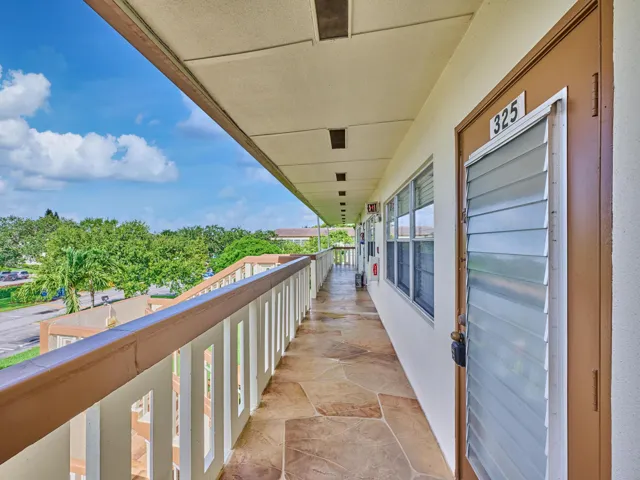 Covered exterior walkway featuring flagstone-style flooring, a railing with decorative cutouts, and views of mature trees