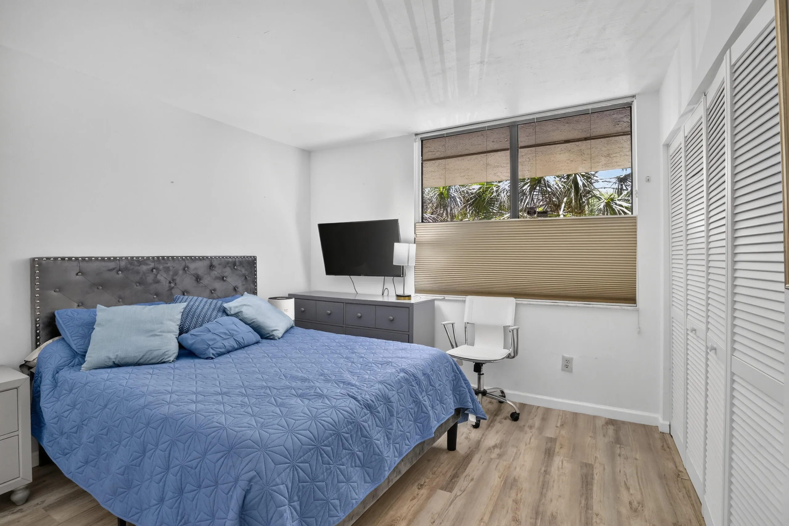 Bedroom featuring wood-finish flooring, a tufted headboard, and dual louvered closet doors