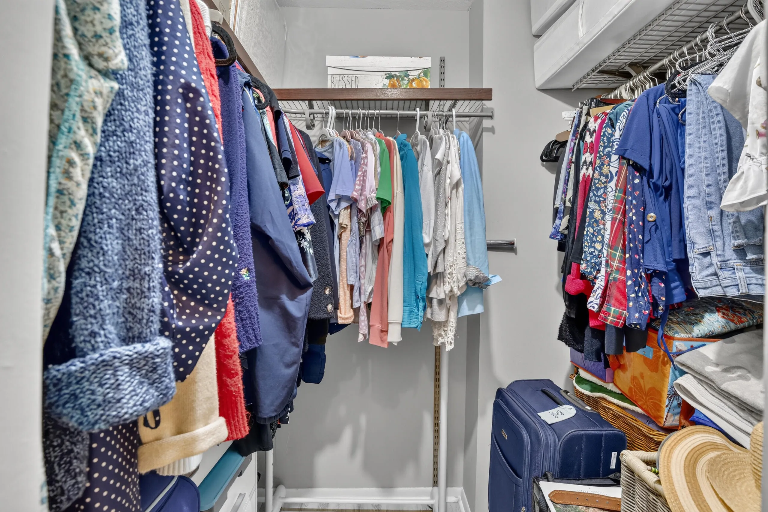 Walk-in closet featuring wire shelving, multiple hanging rods, and an overhead wood-finish shelf