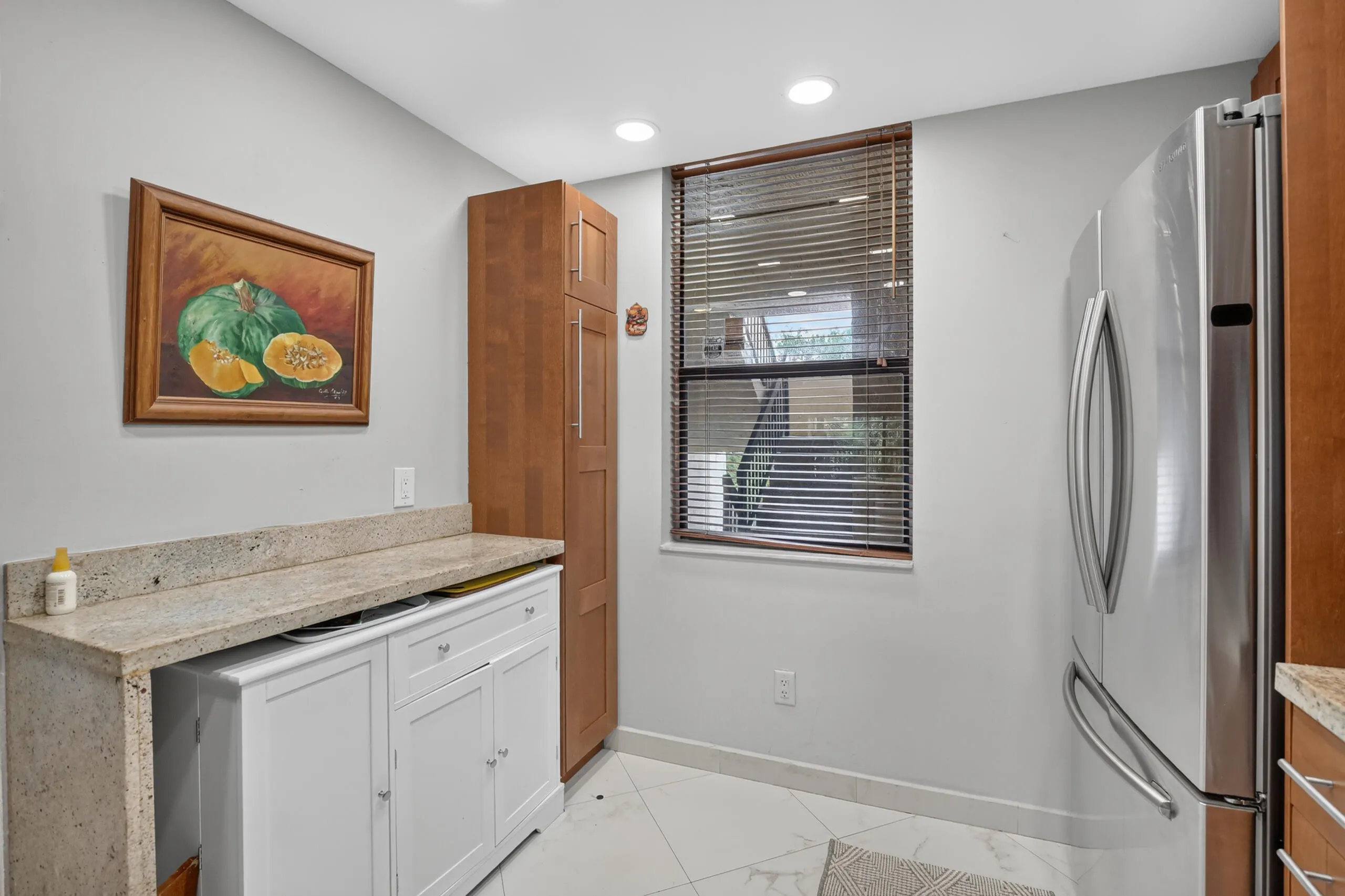 Kitchenette featuring light-toned stone-finish countertops, white cabinetry with silver hardware, and a stainless steel refrigerator