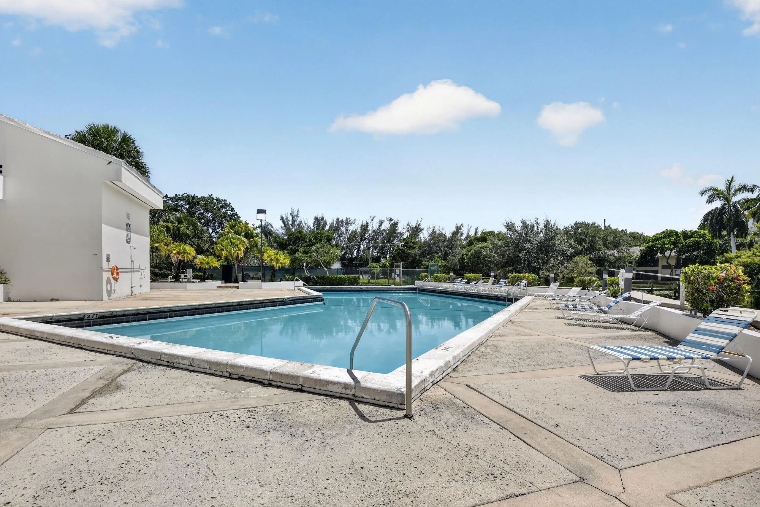 Geometric-shaped outdoor swimming pool featuring a perimeter coping, metal handrails, and surrounding concrete decking
