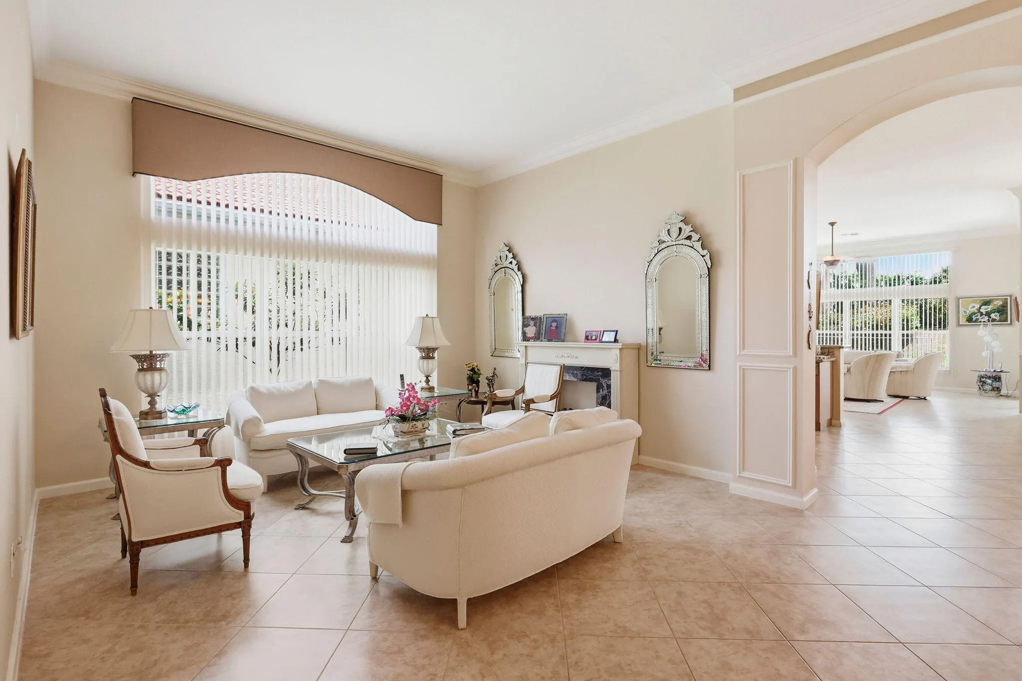 Living room featuring large windows with vertical blinds, tile flooring, crown molding, and an arched entryway