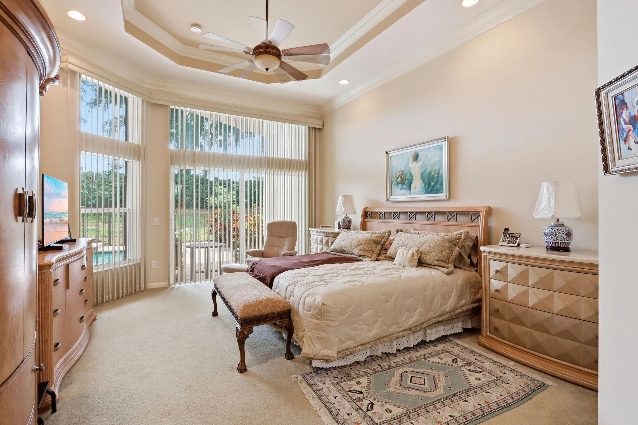 Spacious room featuring a tiered tray ceiling with recessed lighting and a ceiling fan, a large window array with vertical blinds, and soft carpet flooring