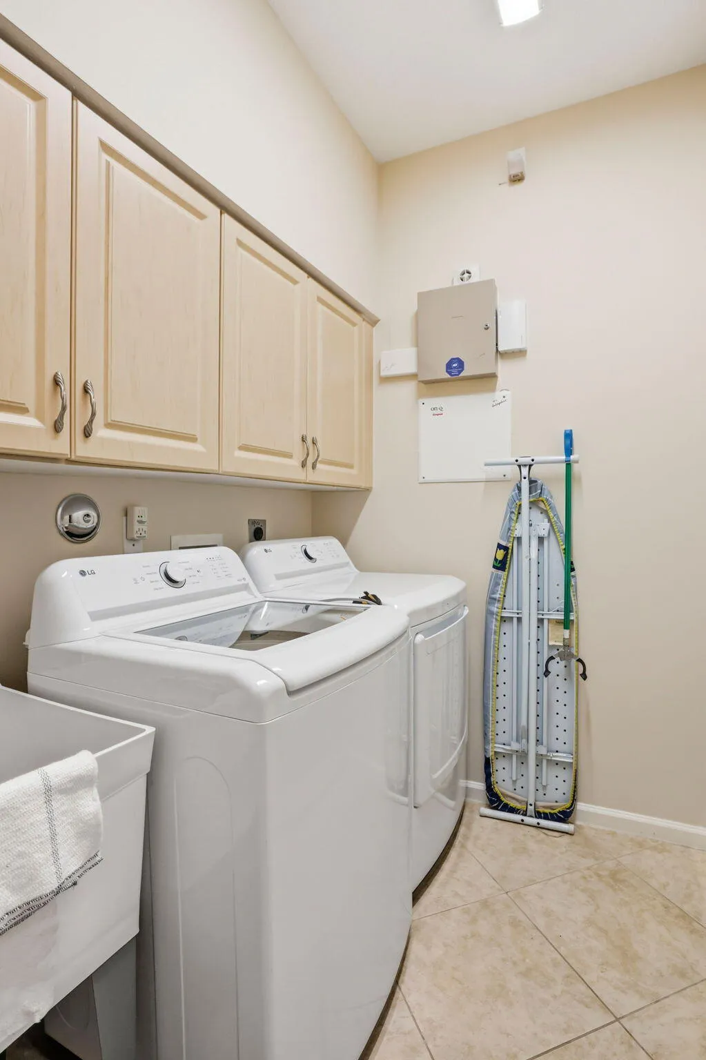 Dedicated laundry area featuring upper cabinetry, a utility sink, and tile flooring