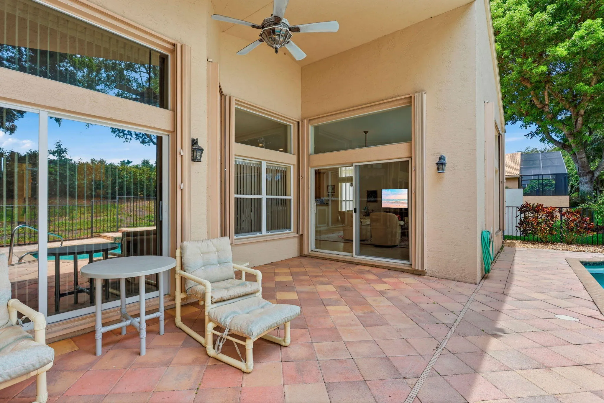 Spacious outdoor patio featuring terracotta-toned paver flooring, a built-in ceiling fan, and multiple exterior wall sconces