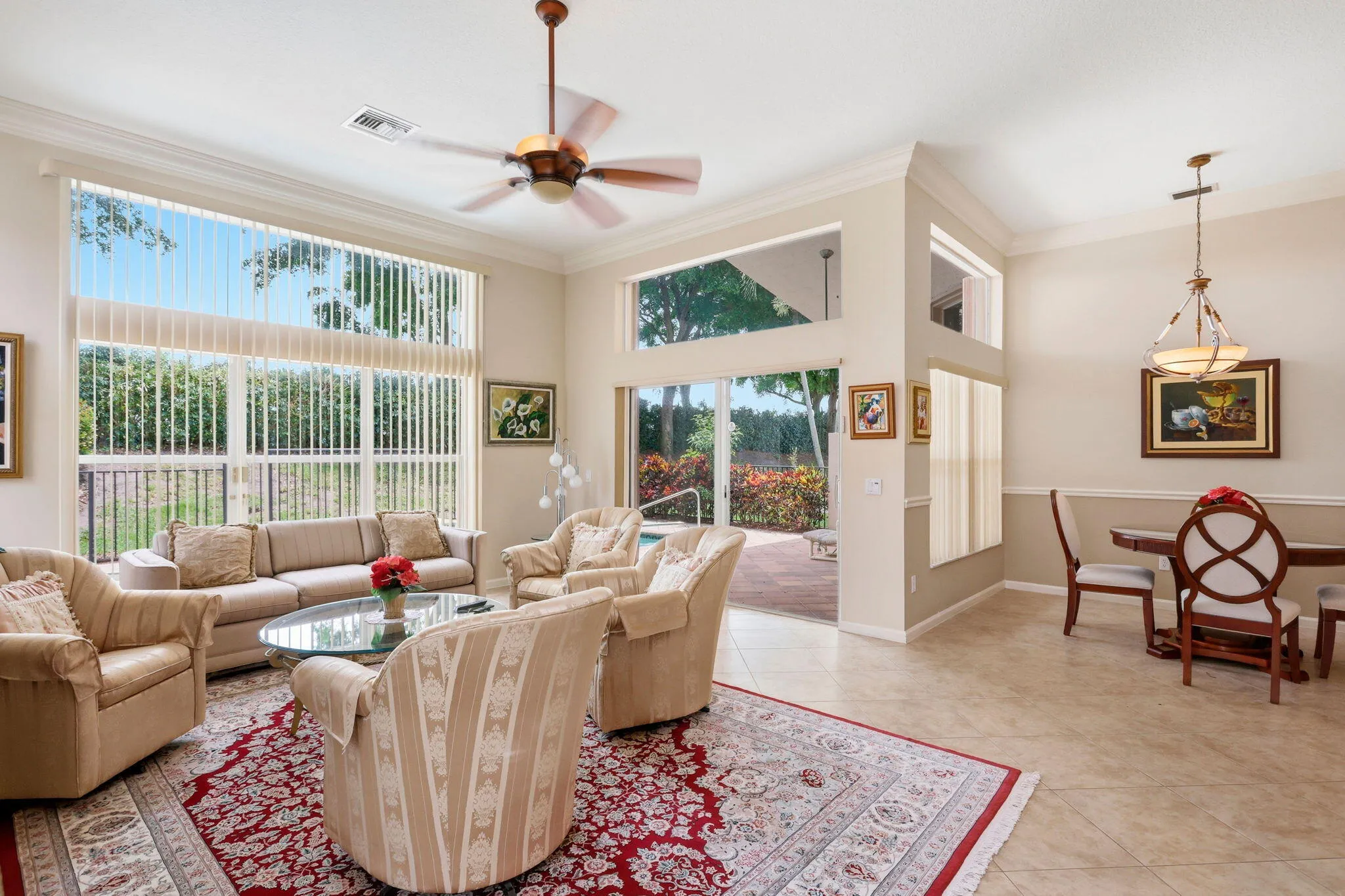 Spacious living area featuring large windows with vertical blinds, a ceiling fan, and tile flooring