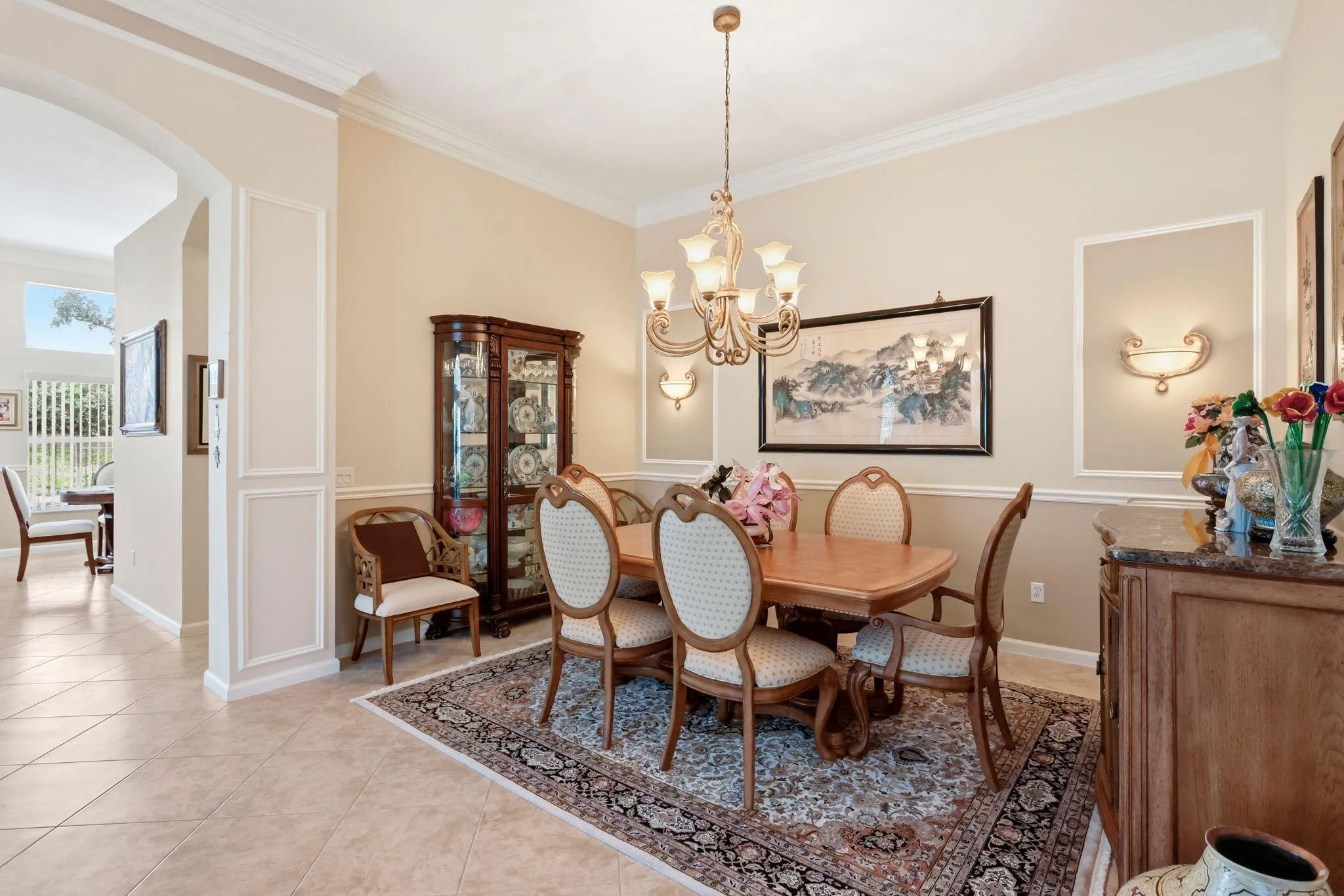Formal dining area featuring tile flooring, crown molding, chair rail detailing, arched doorways, and a decorative chandelier