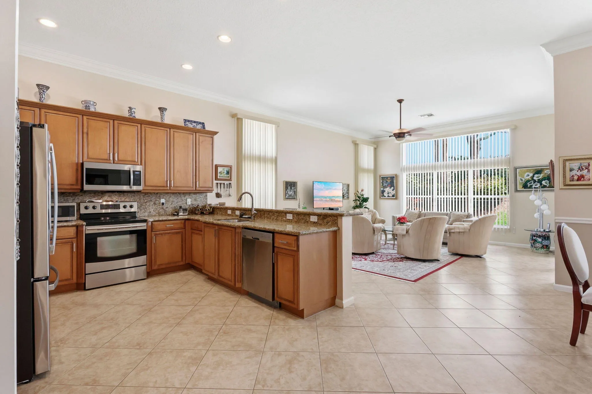 Open-concept living space featuring a kitchen with wood cabinetry, stainless steel appliances, granite countertops, and a tile backsplash