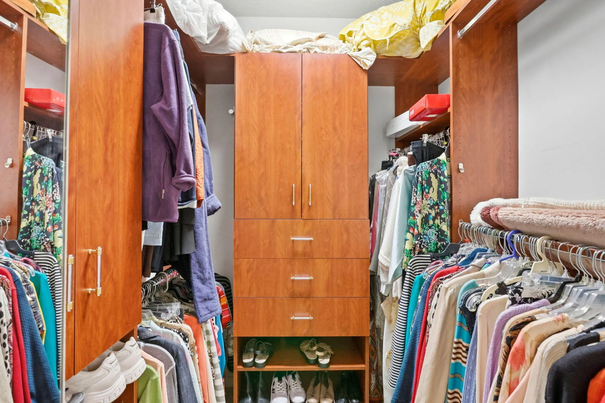 Built-in closet system featuring wood-finish cabinetry, multiple hanging rods, shelving, and drawers