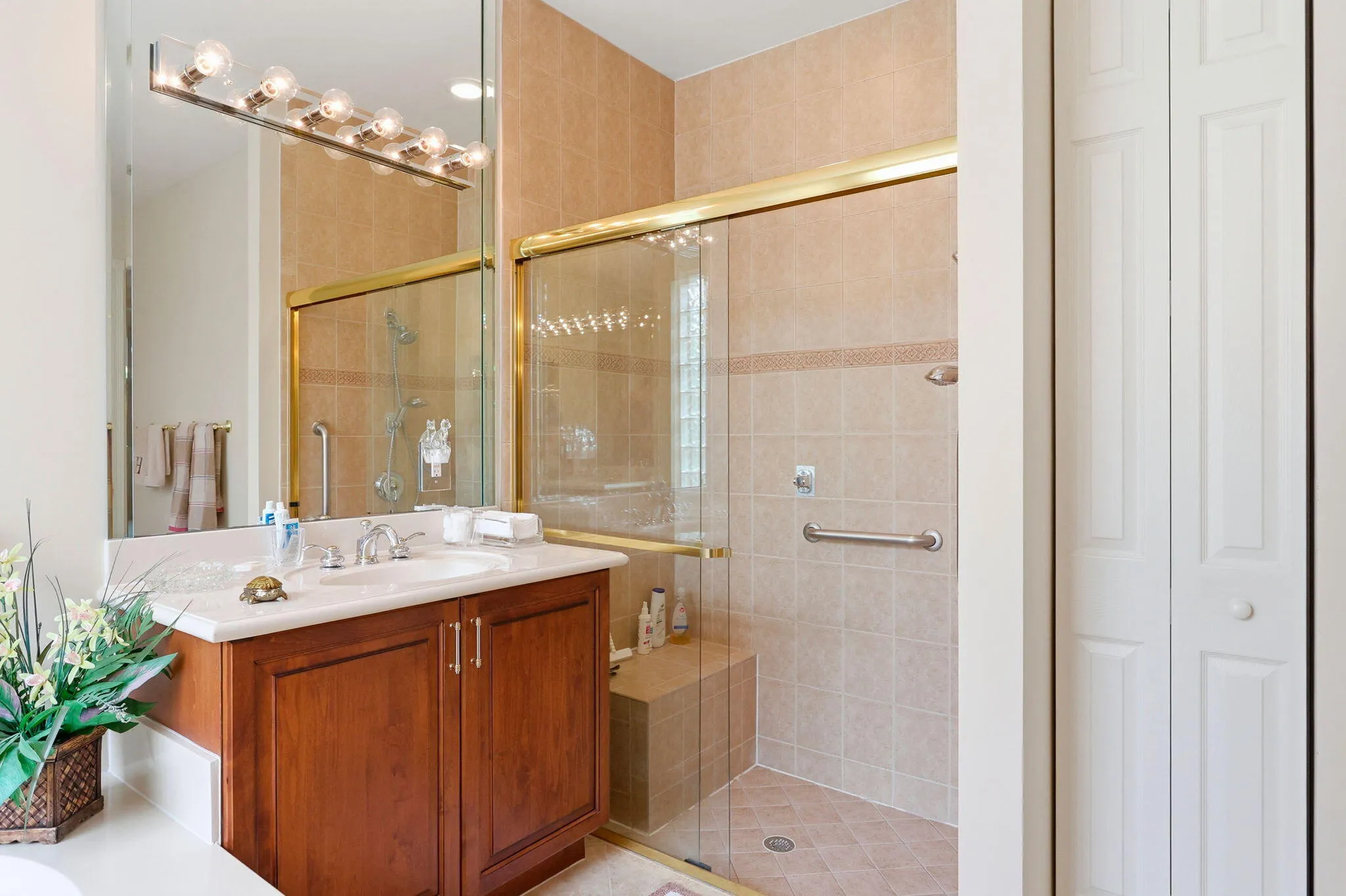 Tiled shower enclosure with glass doors, integrated bench seating, and grab bars