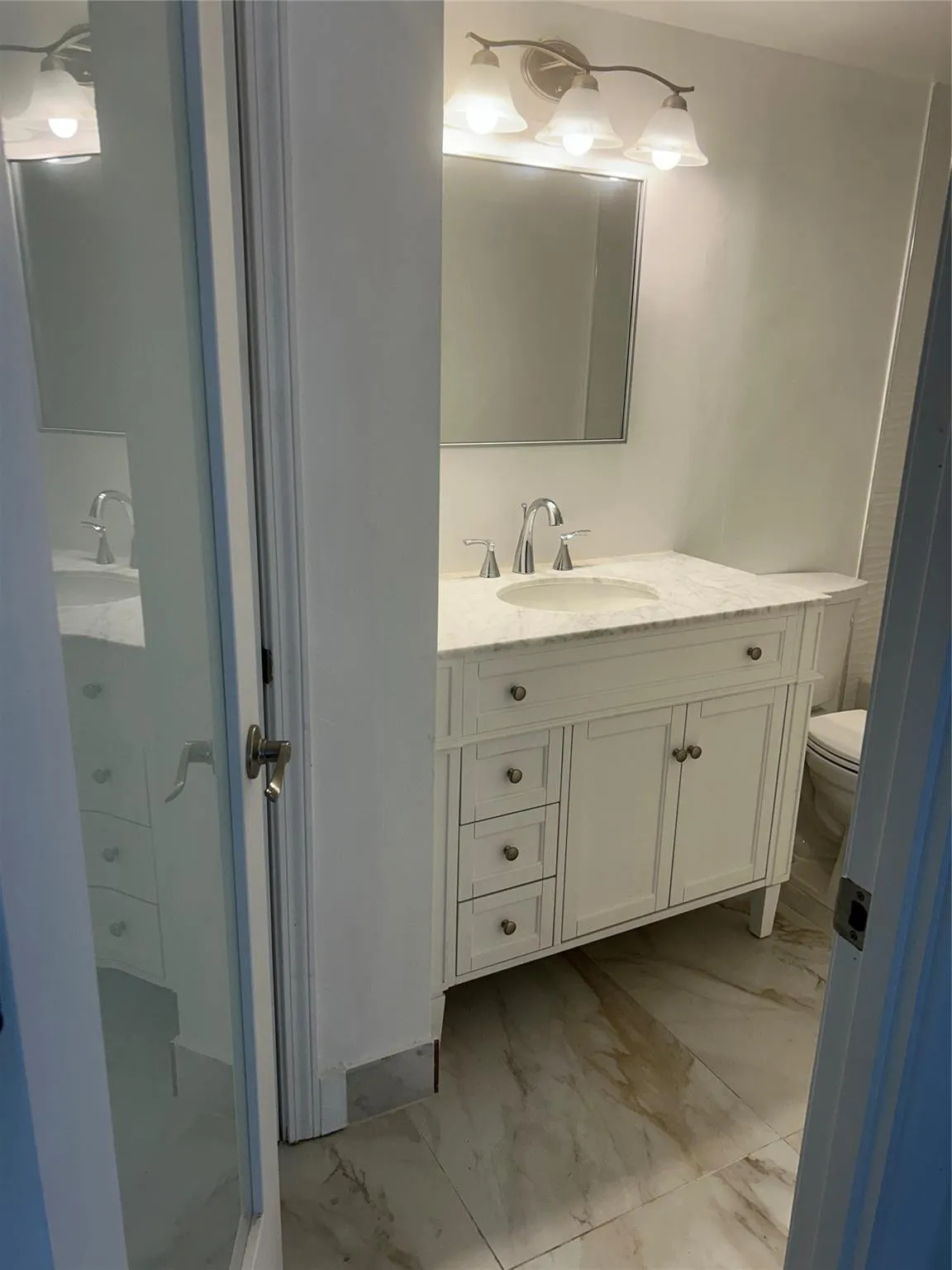 Frosted glass door leads into this bathroom. four shelve storage closet is on the side of the vanity walls with a pre hung door. Ceramic tile flooring and baseboards surround the area.