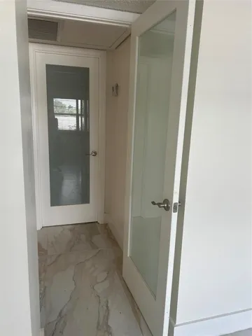 Hallway off the living room where entrance to bedroom and bathroom are separated by frosted glass doors. Th New air-conditioning vent covers are throughout the unit of which one is attached to the ceiling.
