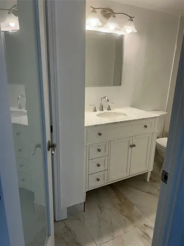 Frosted glass door leads into this bathroom. four shelve storage closet is on the side of the vanity walls with a pre hung door. Ceramic tile flooring and baseboards surround the area.