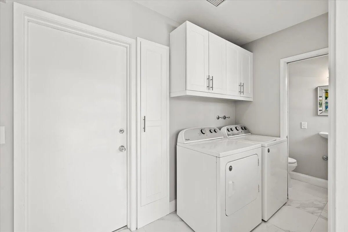 Dedicated laundry area featuring white upper cabinetry, a utility door, and a built-in storage cabinet