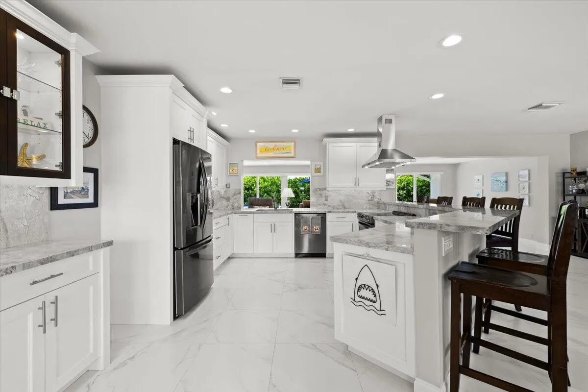 Open-concept kitchen featuring white cabinetry, light-toned countertops with a matching backsplash, stainless steel appliances, and large format tile flooring
