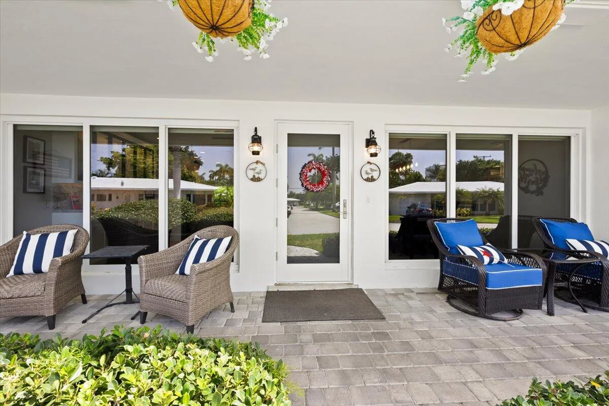Spacious covered patio with light gray paver flooring, multiple large windows, and a glass-paneled entry door