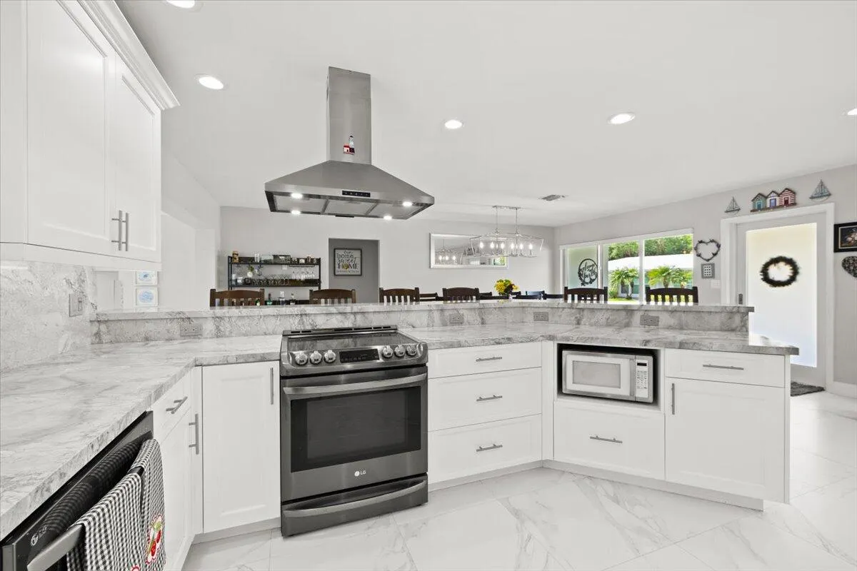 Modern kitchen featuring white cabinetry, light-toned countertops with a matching backsplash, stainless steel appliances including a range with an overhead hood, and recessed lighting
