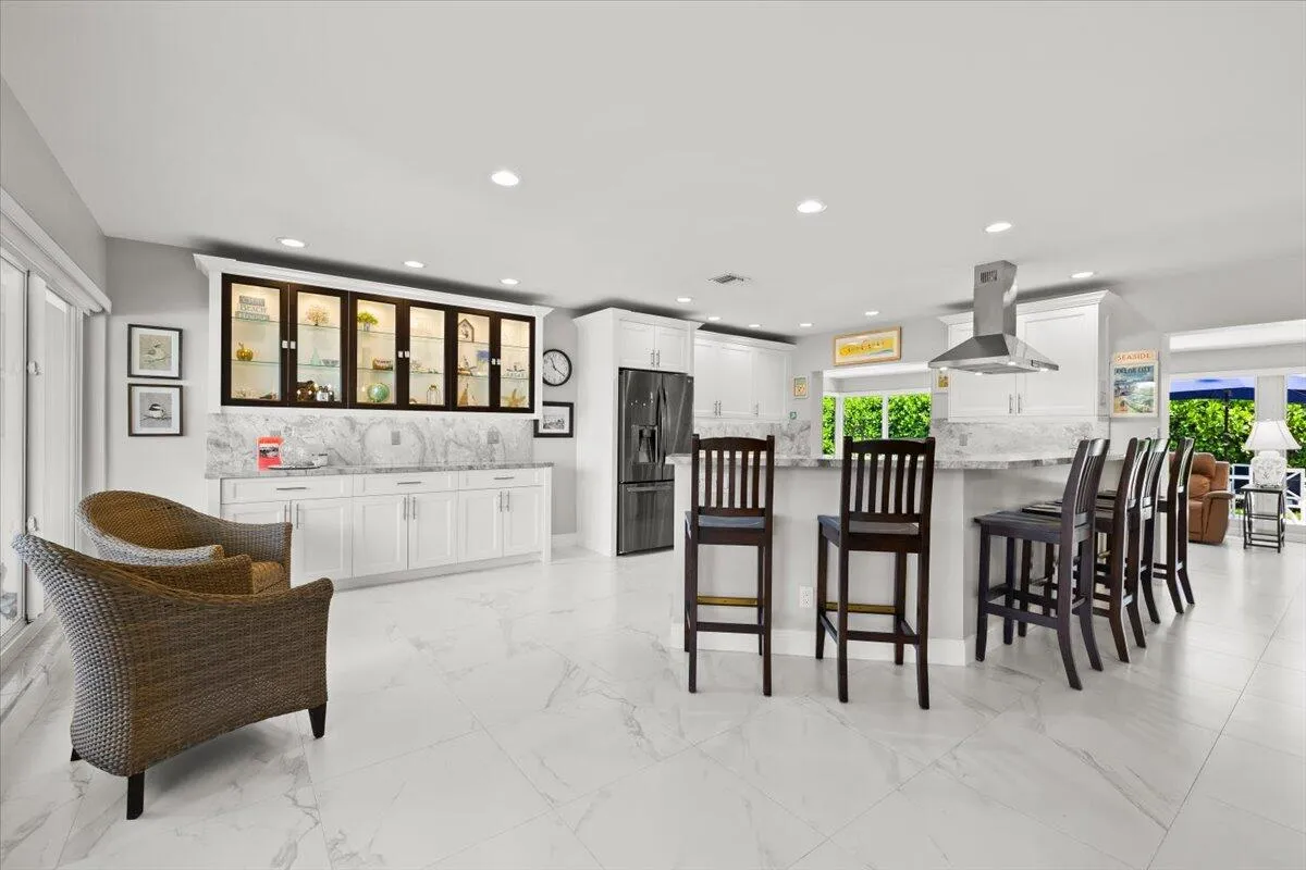 Spacious open-concept kitchen featuring white cabinetry, a large island with seating, a stainless steel range hood, and a built-in display cabinet with glass doors