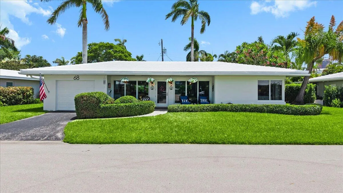 Single-story residence featuring a white exterior, attached garage, and a lush, manicured lawn with mature palm trees