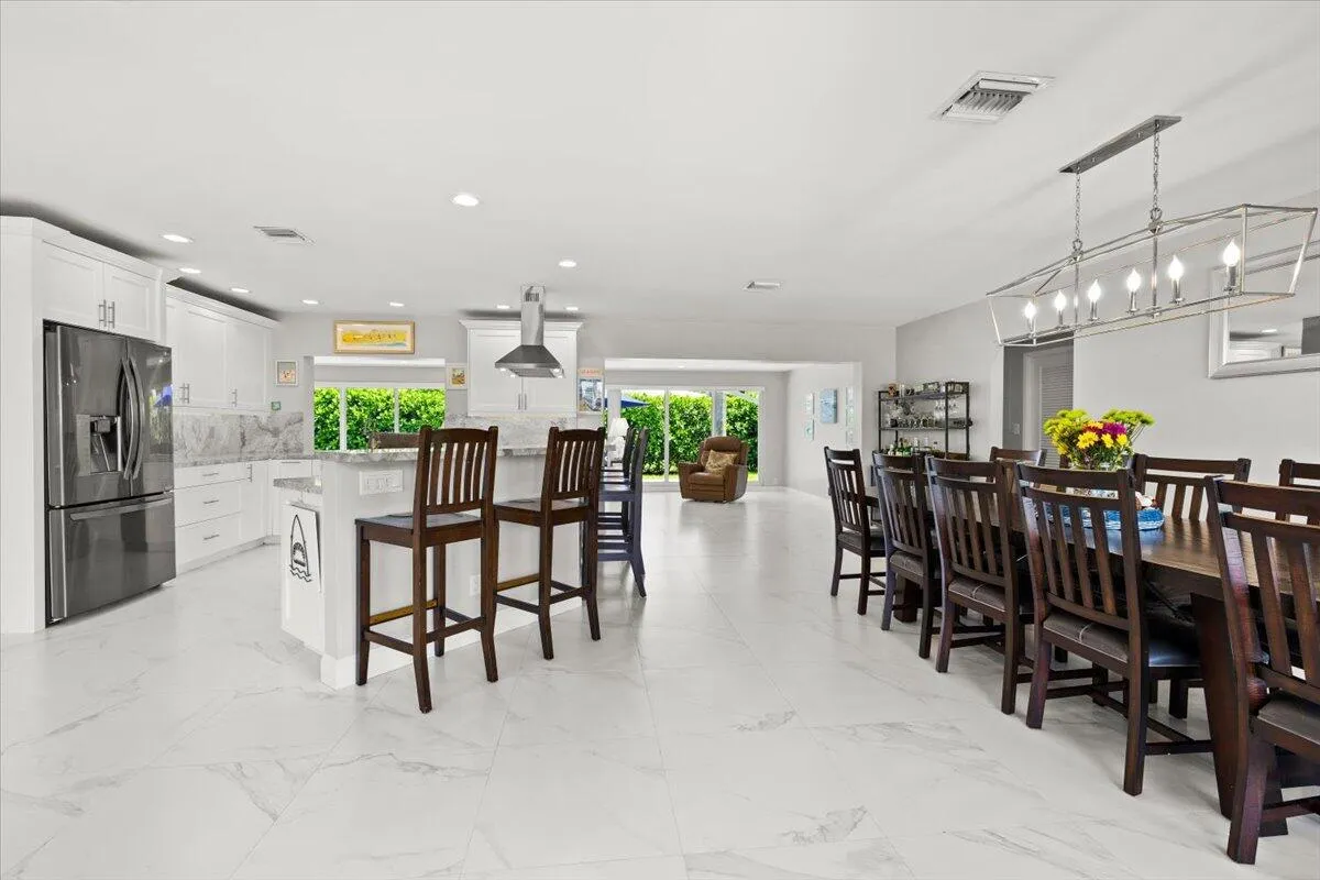Open-concept kitchen and dining area featuring large format tile flooring, white cabinetry, a kitchen island with seating, stainless steel appliances, and a dining area with a linear chandelier