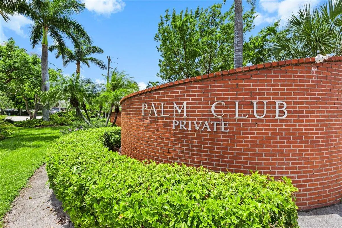 Brick wall entrance signage for "Palm Club Private" featuring lush green landscaping