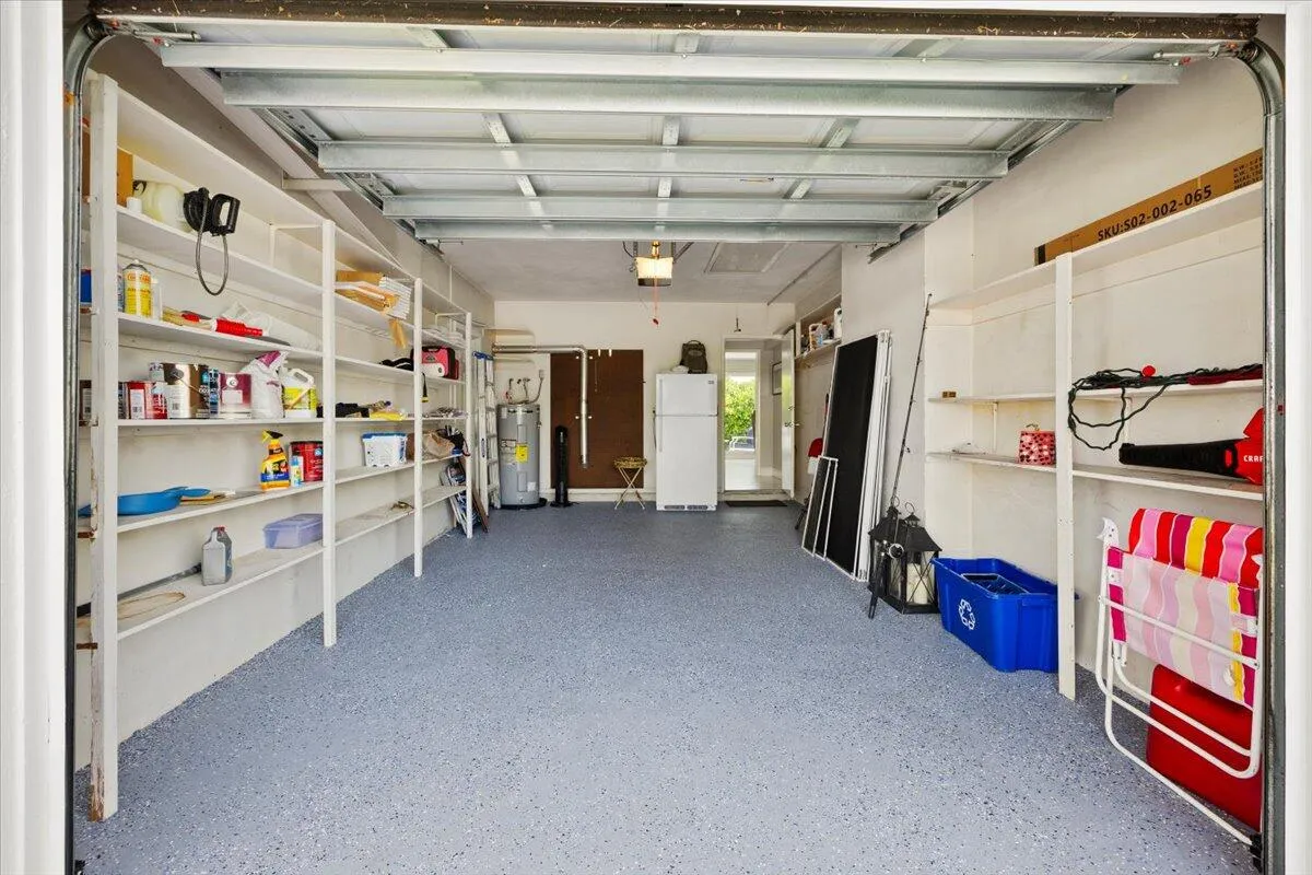 Spacious garage with textured gray flooring, extensive built-in shelving, white painted walls, and exposed ceiling joists