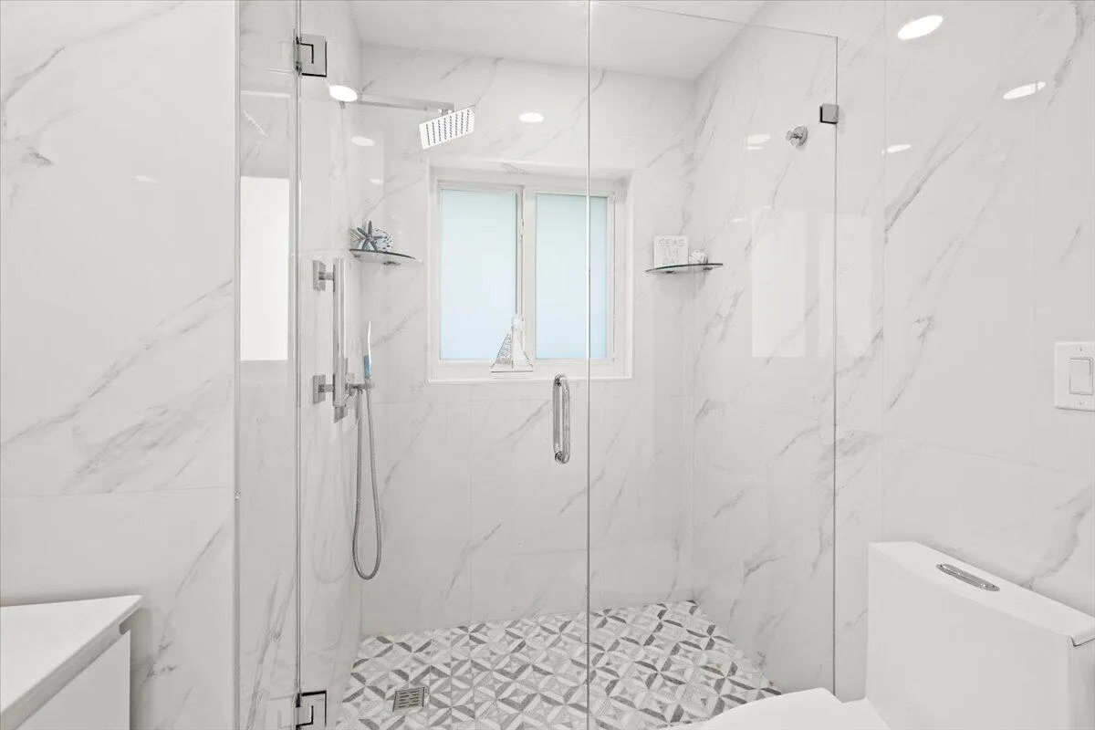 Walk-in shower featuring a frameless glass enclosure, rain shower head, hand-held shower, patterned floor tiling, and large-format wall tiles