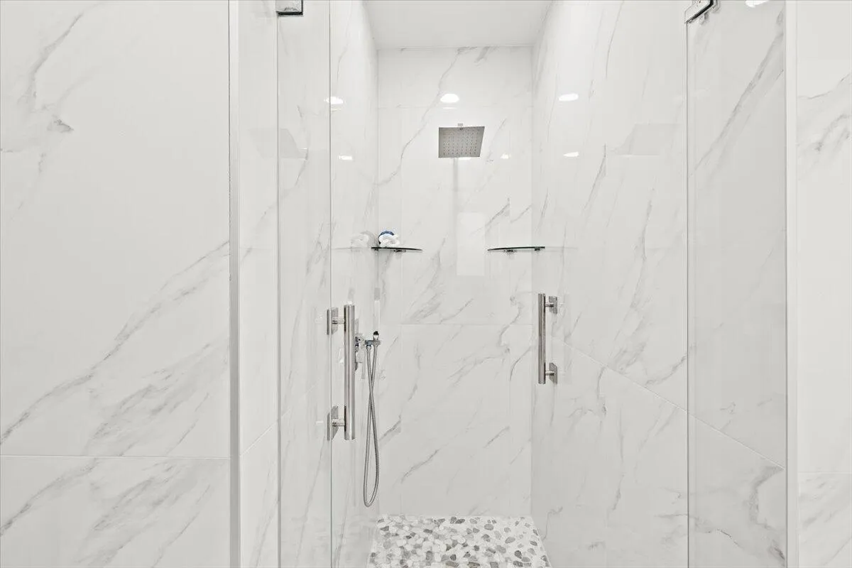 Spacious shower enclosure with floor-to-ceiling marble-look wall tiles, a rainfall showerhead, and glass doors with chrome hardware