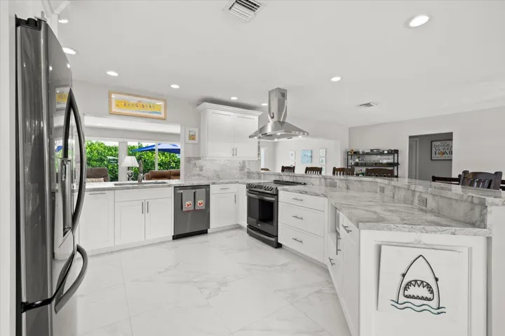 Expansive kitchen featuring white cabinetry, light-toned stone countertops, and a large curved island