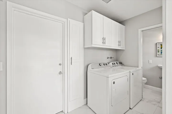 Dedicated laundry area featuring white upper cabinetry, a utility door, and a built-in storage cabinet