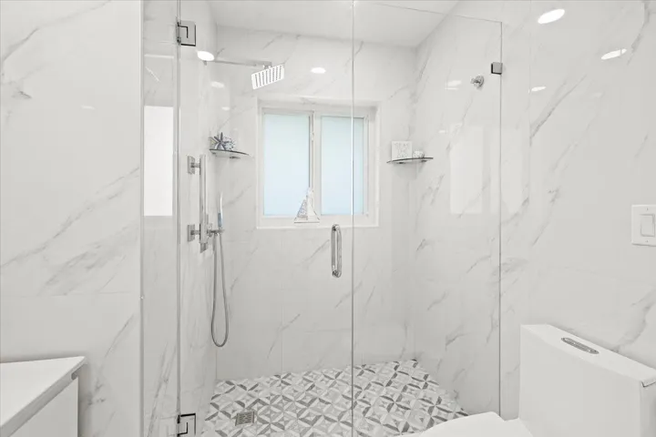 Walk-in shower featuring a frameless glass enclosure, rain shower head, hand-held shower, patterned floor tiling, and large-format wall tiles