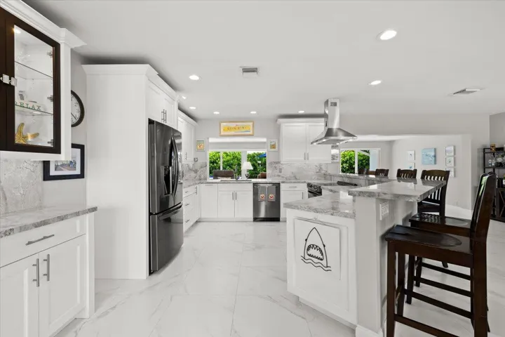 Open-concept kitchen featuring white cabinetry, light-toned countertops with a matching backsplash, stainless steel appliances, and large format tile flooring