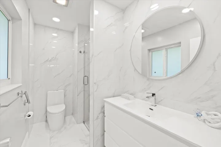 Bathroom featuring a white floating vanity with an integrated sink and chrome faucet, a circular wall-mounted mirror, and a frameless glass shower enclosure