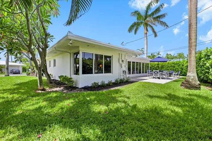 Manicured lawn surrounding a contemporary white stucco residence with multiple large windows and a spacious outdoor patio