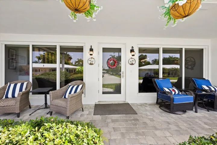 Spacious covered patio with light gray paver flooring, multiple large windows, and a glass-paneled entry door