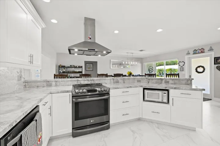 Modern kitchen featuring white cabinetry, light-toned countertops with a matching backsplash, stainless steel appliances including a range with an overhead hood, and recessed lighting