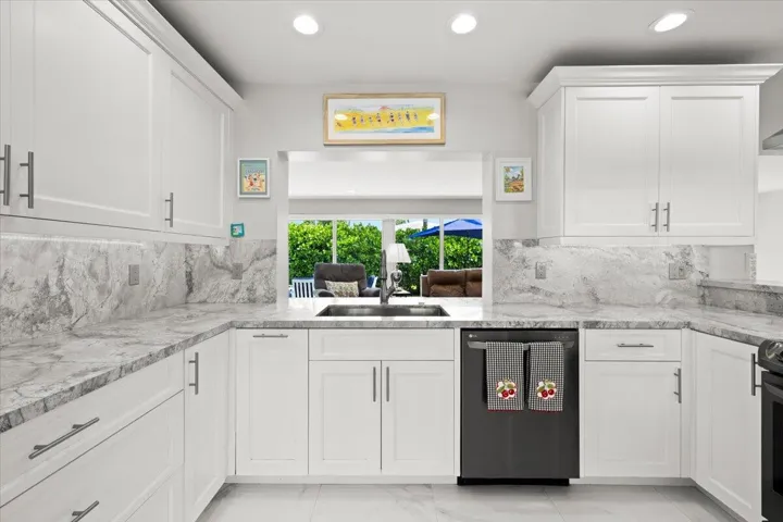 Contemporary kitchen featuring white cabinetry with brushed nickel hardware, light grey stone countertops, a matching full-height backsplash, and recessed lighting