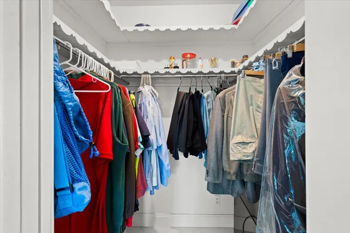 Built-in closet with scalloped trim shelving and white painted walls