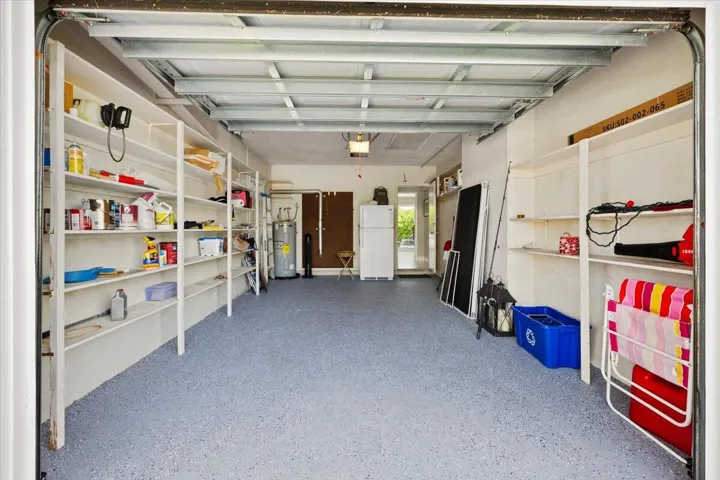 Spacious garage with textured gray flooring, extensive built-in shelving, white painted walls, and exposed ceiling joists