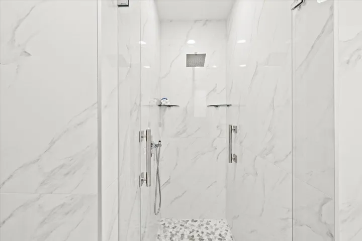 Spacious shower enclosure with floor-to-ceiling marble-look wall tiles, a rainfall showerhead, and glass doors with chrome hardware