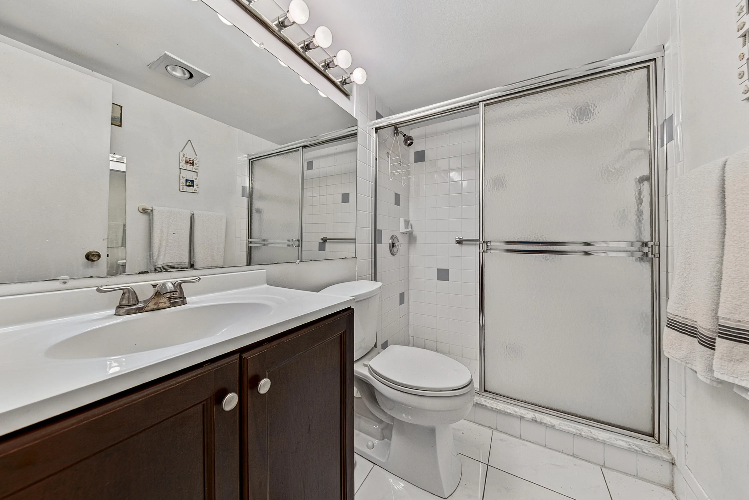 Bathroom featuring a dark wood-finish vanity with a white integrated sink, a full-width mirror, and a shower enclosure with frosted sliding glass doors