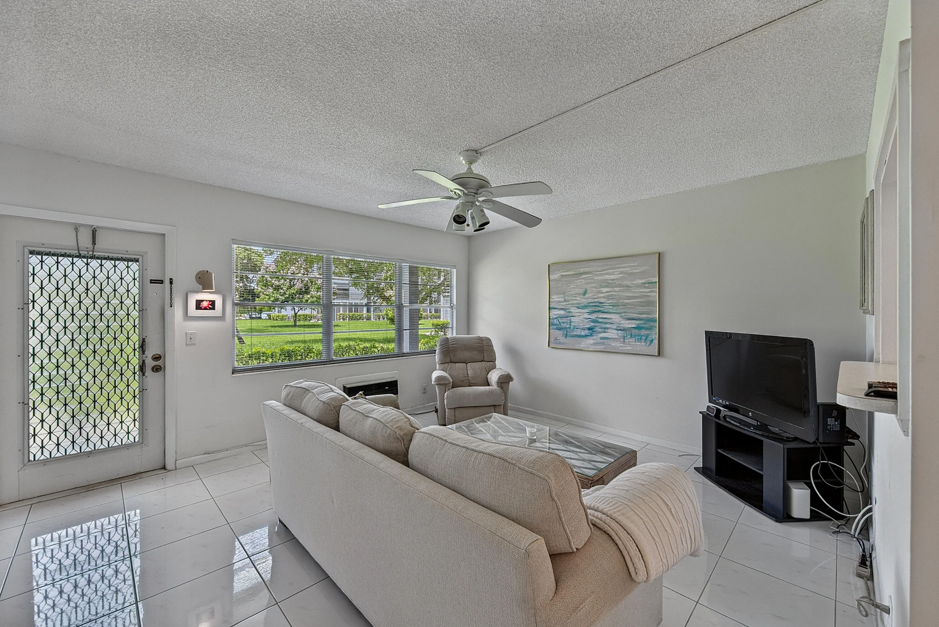 Bright living area featuring white tile flooring, a large window with exterior views, and a ceiling fan