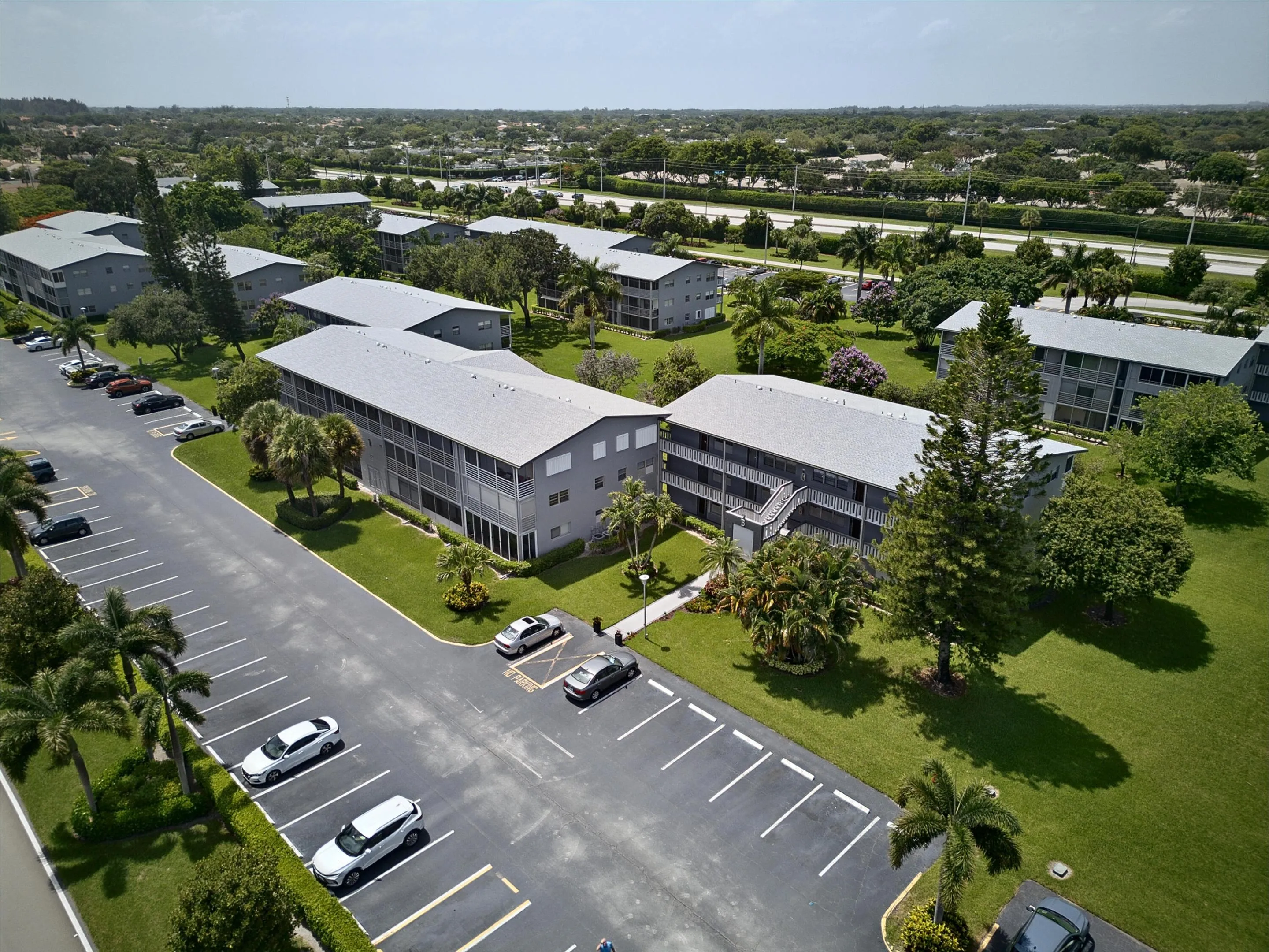 Multi-story residential buildings with screened balconies, surrounded by mature landscaping and paved parking areas