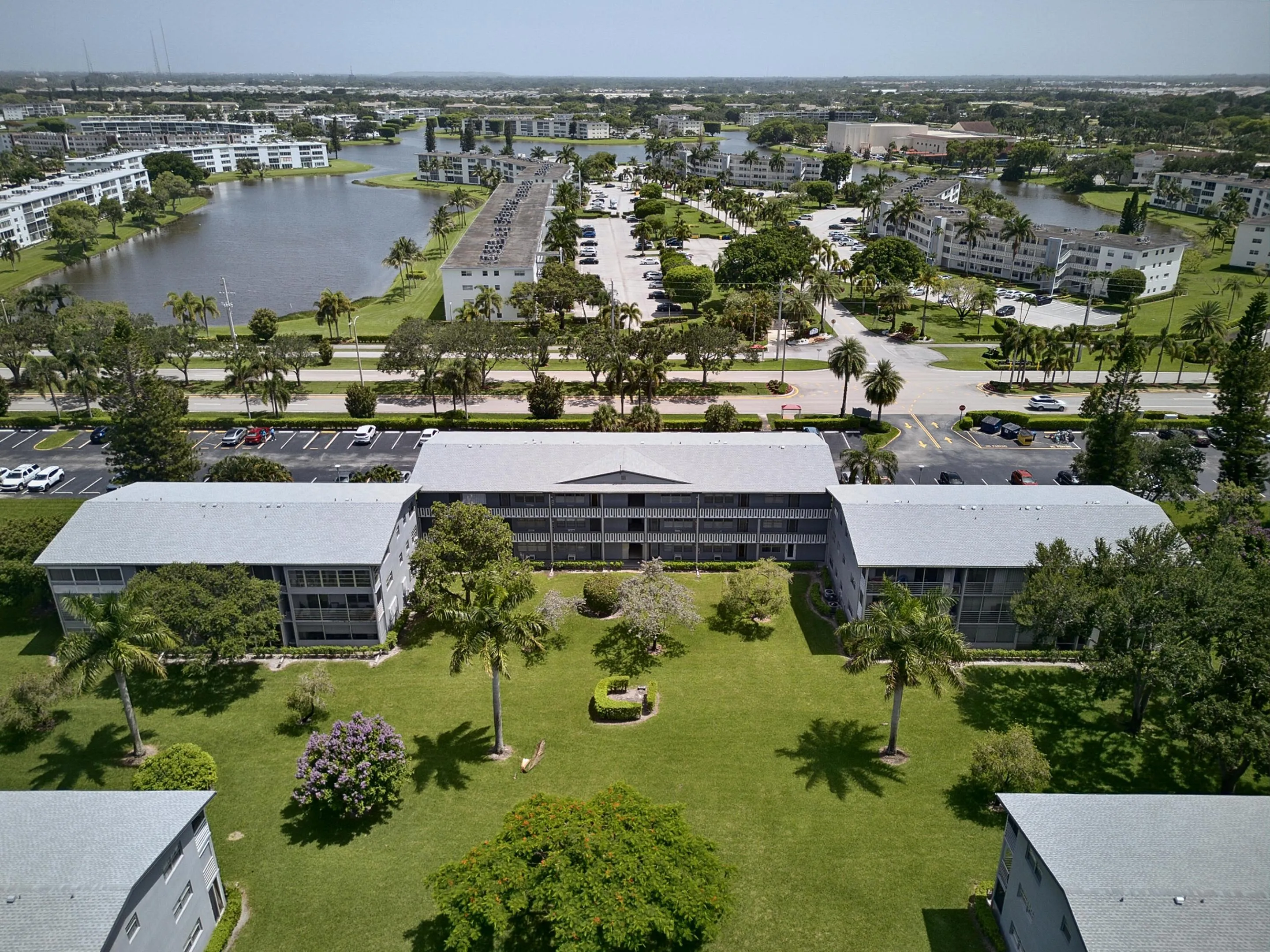 Multi-story residential building featuring a light gray exterior, multiple screened balconies, and a central landscaped courtyard